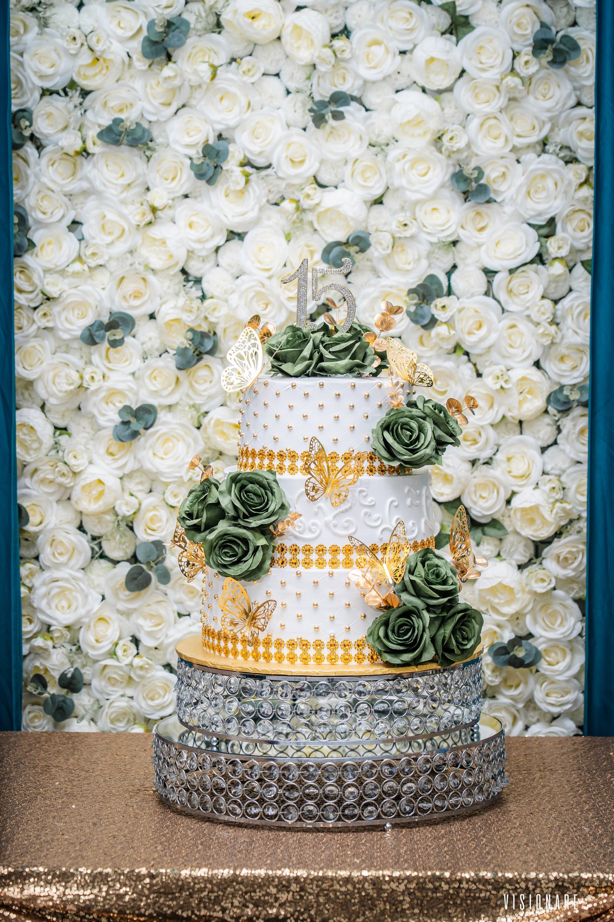 Pastel de quinceañera de tres pisos con flores verdes y mariposas doradas